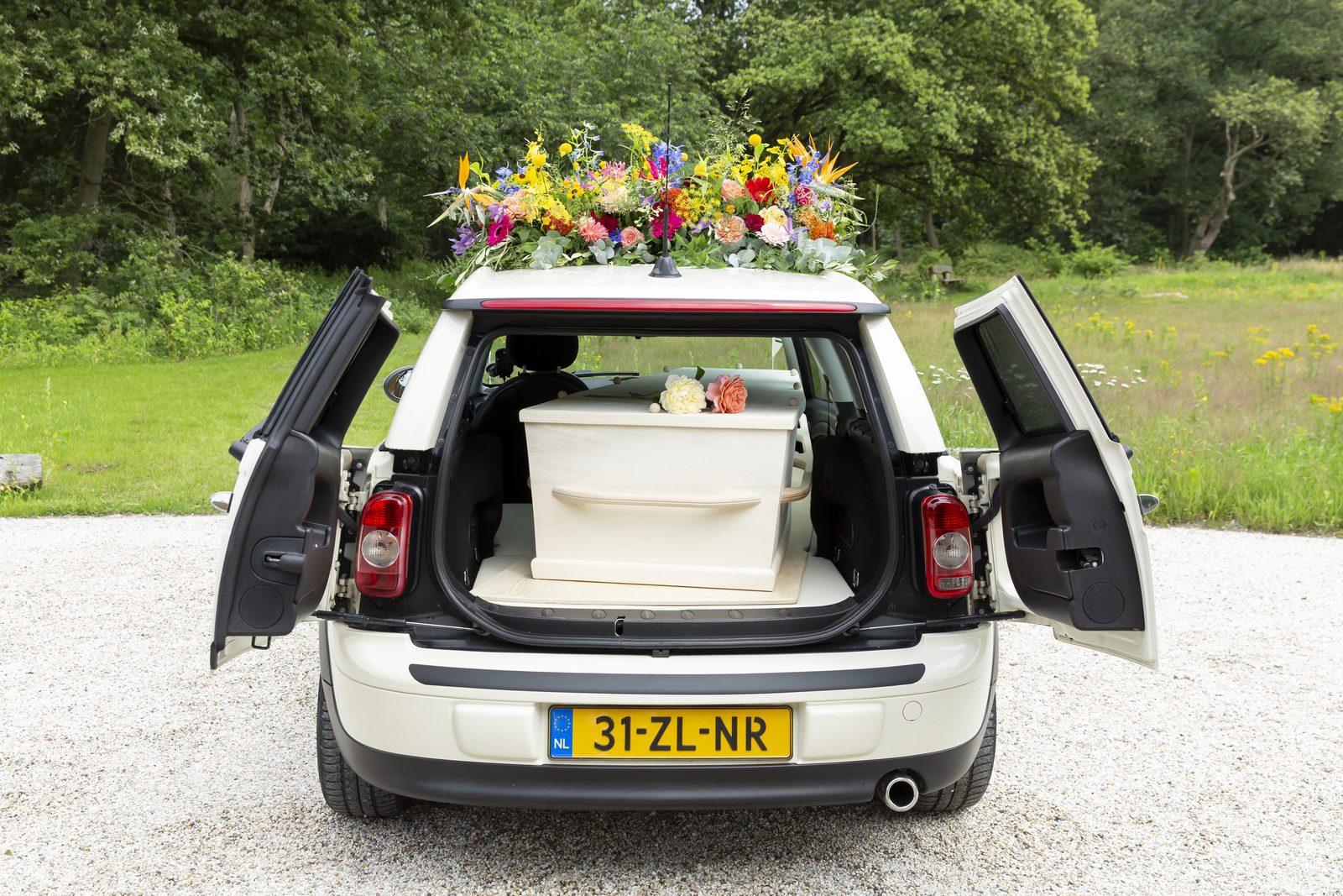 De Minirouwauto met open achterdeuren, een lichte kist en een bloemstuk op het dak
