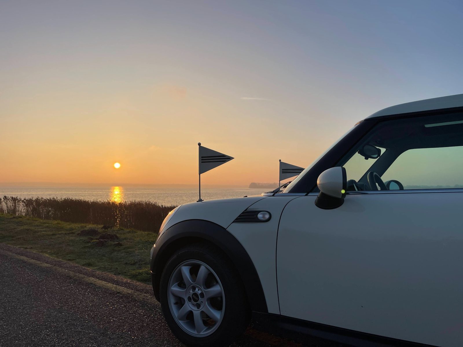 De Minirouwauto met vlaggetjes langs het water bij zonsondergang