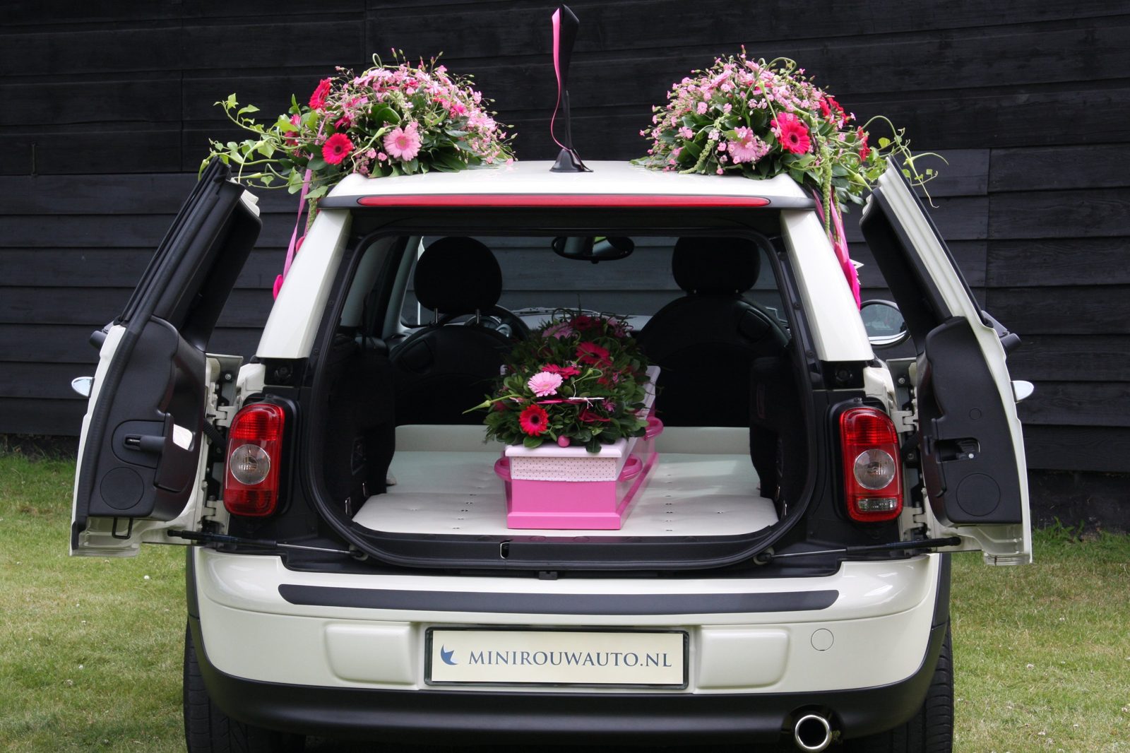 Een roze kinderkistje met bloemen in de Minirouwauto, met bloemstukken op het dak