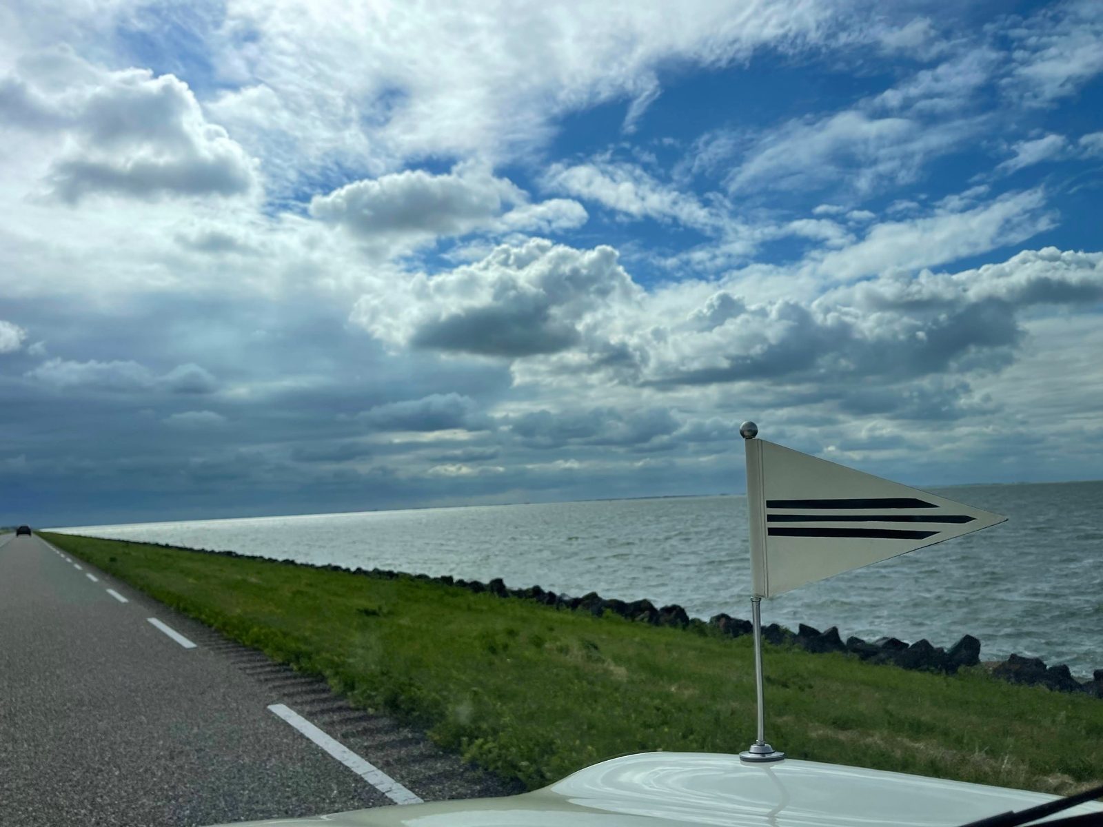 Uitzicht vanuit de Minirouwauto over de dijk, met het vlaggetje op de motorkap